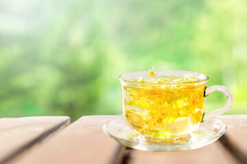 Herbal tea from linden flowers in a cup on a wooden table against the background of nature. 