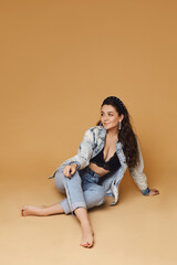 Caucasian young woman with wavy hair in denim clothes, isolated on beige. Model girl in a modish outfit at the beige background