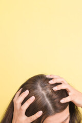 Naklejka premium The woman shows gray hair on her head. Hair with fragments of gray hair requiring coloring on a yellow background with copy space