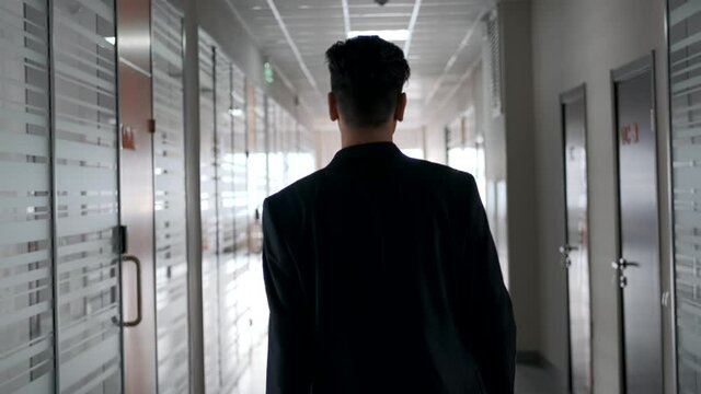 A young employee in an office suit walks down a narrow corridor. Slow motion.