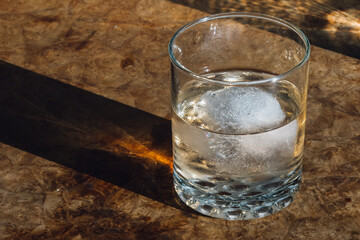 light pink liquid water glass with ice on burl wood table in sun with hard shadow 