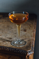 elegant whiskey cocktail in hollow stem coupe glass on burl wood table still life 