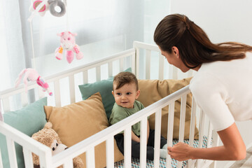 Obraz na płótnie Canvas Smiling kid sitting in baby bed near mother