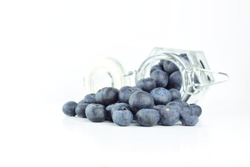 Blueberries scattered and inside a glass jar lying, on white background.