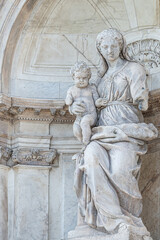 Ancient, aged sculpture of beautiful Venetian Renaissance Era woman, a mother with a child in her hands at Basilica San Marco in Venice, Italy.