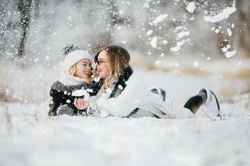 Front view of beautiful mother and her little adorable daughter lying on the snow and have fun...