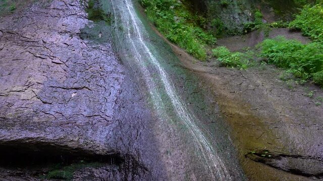 Wasser eines Wasserfalls fließt über eine teils bewachsene Felswand