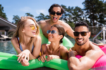 Obraz premium cheerful multiethnic friends having fun on inflatable mattress in swimming pool