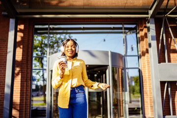 Young african american woman wearing yellow blouse smiling happy dancing listening to music using headphones drinking coffee at the city street outdoor.