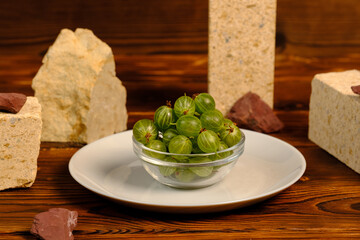 green gooseberries in a transparent bowl on a white plate.