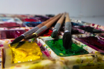 Obraz premium four brushes on a background of multi-colored watercolor paint taken in macro shooting