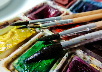 Obraz premium four brushes on a background of multi-colored watercolor paint taken in macro shooting