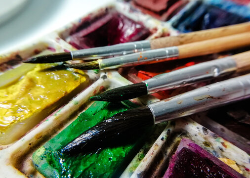 four brushes on a background of multi-colored watercolor paint taken in macro shooting