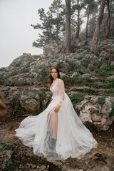 A bride in a white dress stands in the misty mountain forest. 