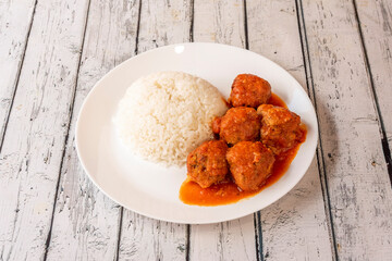 Plate of meatballs in tomato sauce with white rice garnish on white plate and white table