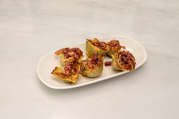Tray with a portion of fried artichoke hearts with a lot of salt and pieces of Serrano ham on white...