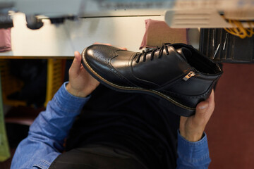Man holding black leather boot. Close up shot from above of new stylish footwear in hands of shoe...