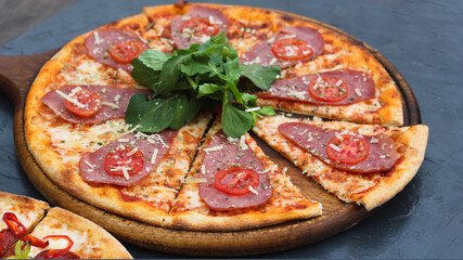Delicious Italian pizza with smoked meat and tomatoes, with arugula leaves.