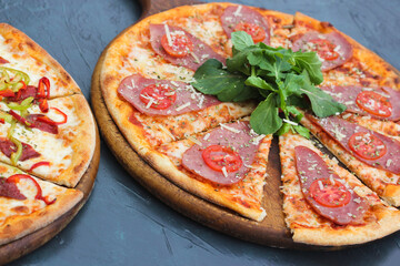 Delicious Italian pizza with smoked meat and tomatoes, with arugula leaves.