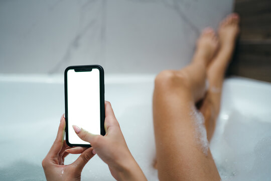Photo of a girl lying in a bathtub and holding a phone with a screen in her hands. Space for text
