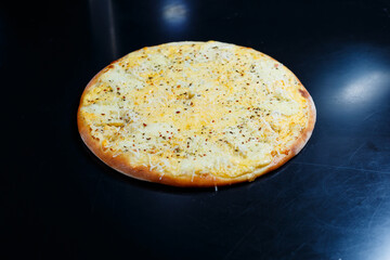 Delicious Four Cheeses pizza with cheddar, parmesan, mozzarella and tomato sauce on a black background. View from above.