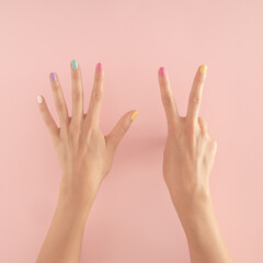 women hands with colorful nails on the pastel pink background. copy space.  summer modern tropical abstract art with female hand. minimal background idea with number seven