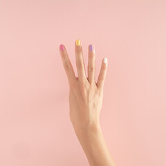 women hands with colorful nails on the pastel pink background. copy space.  summer modern tropical abstract art with female hand. minimal background idea with number four