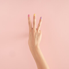 women hands with colorful nails on the pastel pink background. copy space.  summer modern tropical abstract art with female hand. minimal background idea with number three