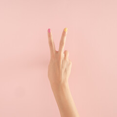 women hands with colorful nails on the pastel pink background. copy space.  summer modern tropical abstract art with female hand. minimal background idea with number two