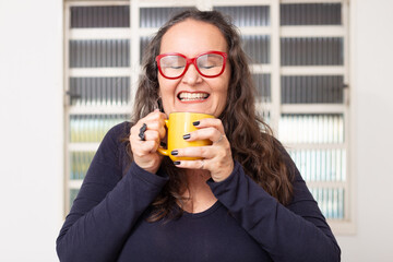 Mulher feliz usando óculos vermelhos e segurando uma caneca amarela.