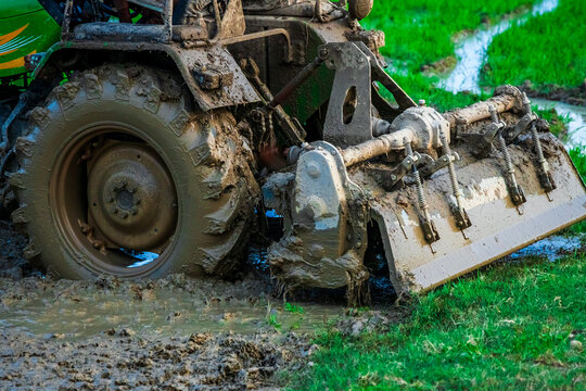 Tractor ploughs field. Close up shot of heavy machinery attached to the rear end of tractor covered in mud ploughs through the muddy field.