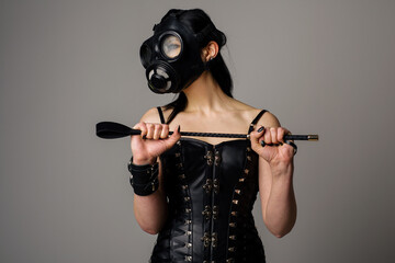Sensual woman in black leather corset with gas mask and riding crop in hand