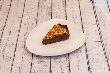 Portion of homemade chocolate cake with chopped nuts on top on white plate
