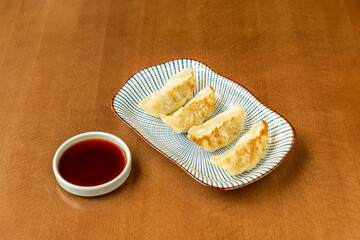 Chinese dumplings stuffed with vegetables cooked on the grill on a plate decorated with blue lines and a small container with soy sauce