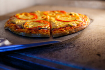 Hot tasty American pizza with tomato cheese and meat with a thick crust on a metal shovel, the baker takes out the pizza from the oven