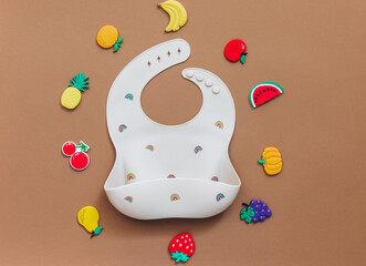 Cute baby bib for food on brown light background, top view, copy space, Bright baby tableware, first food concept, flat lay, copy space
