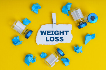 On a yellow background are ampoules, blue crumpled paper and paper with the inscription - WEIGHT LOSS