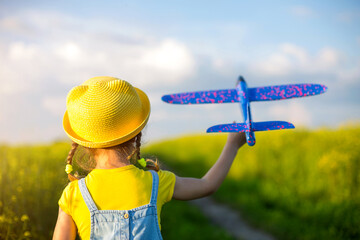 Girl in a yellow hat launches a toy plane into the field, looks at the trail. Summer time,...