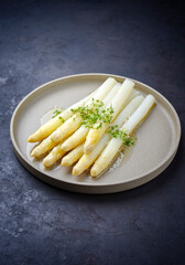 Modern style traditional steamed white asparagus with butter sauce hollandaise and cress served as close-up on a Nordic design plate