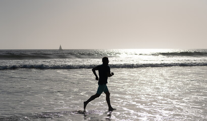 Fototapeta na wymiar athletic man runner silhouette run on summer beach with sea water and sun, endurance