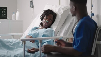 A black male doctor is talking to a black female patient lying on a hospital bed and connected to an acid supply. The attending physician discusses with the patient in the hospital the treatment
