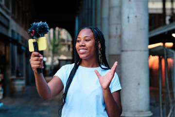 young gen z latin woman streaming outdoors for social media using smartphone and microphone