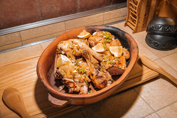 Homemade grilled chicken with spices cut into pieces in red ceramic baking dish on wooden board.