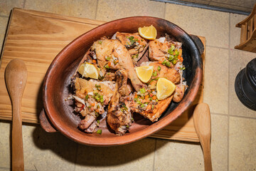 Homemade grilled chicken with spices cut into pieces in red ceramic baking dish on wooden board.