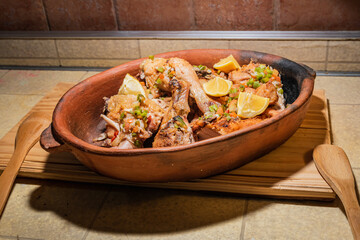 Homemade grilled chicken with spices cut into pieces in red ceramic baking dish on wooden board.