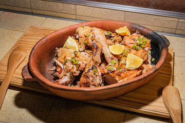 Homemade grilled chicken with spices cut into pieces in red ceramic baking dish on wooden board.