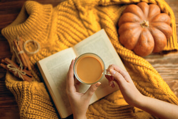 Vintage book with romantic stories and fairy tales. Top view of autumn composition with book and knitted sweater. Hot cocoa in hands, ripe pumpkin, warm sweater and open book on wooden background. 