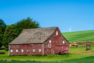 Fototapeta na wymiar Rustic wooden red barn with modern wind turbines in the background seen from rural farming area 