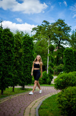 Fototapeta na wymiar Young beautiful sporty blonde woman in a black T-shirt and in black tight sports shorts in good shape posing in front of green trees
