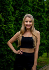 Obraz na płótnie Canvas Young beautiful sporty blonde woman in a black T-shirt and in black tight sports shorts in good shape posing in front of green trees